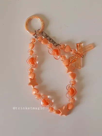 This pastel orange beaded charm is full of hearts, stars, and a cute bow. It's a warm and cheerful accessory that's sure to brighten your day.