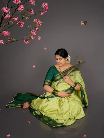 A serene portrait with a touch of symbolism. The mom-to-be holds a peacock feather, often associated with grace and divinity, complementing her beautiful green saree.