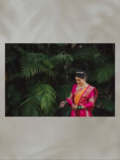 A portrait of the bride in her navari sari, set against a backdrop of lush green leaves.