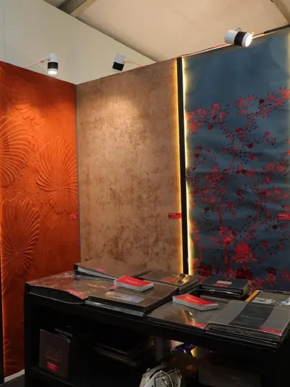 A display of our textured and 3D wallcoverings at a design event. The image showcases a variety of finishes, from a deep red floral relief to a shimmering metallic texture, highlighting the diversity of our collection.
