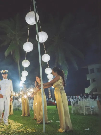 A beautiful night shot of the couple's entrance at their reception. The bridesmaids hold sparklers under a string of paper lanterns, creating a dreamy and festive scene.