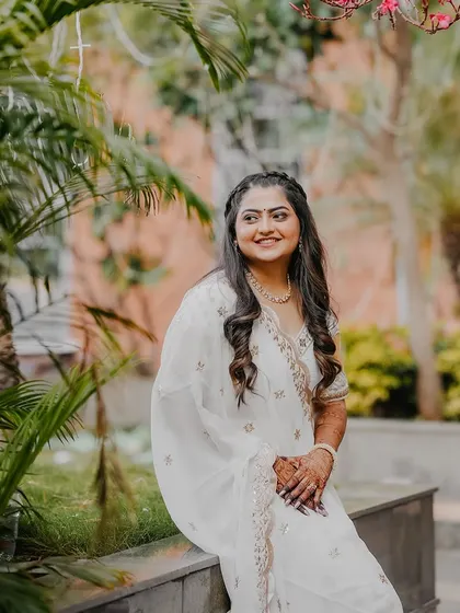 A beautiful portrait of the bride in her white Haldi outfit, seated in a garden setting. Her serene smile captures the peaceful joy of the morning.