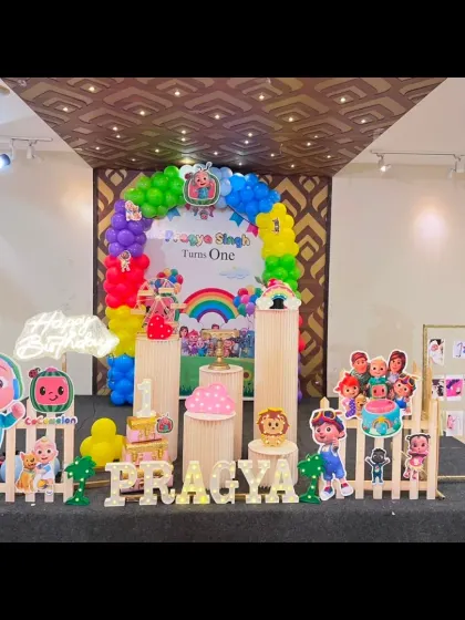 A vibrant Cocomelon themed birthday party setup. This decor features a rainbow balloon arch, multiple character standees, and custom lettering for a colorful and fun celebration.