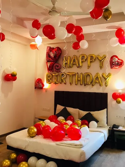 A romantic birthday room decoration. The bed is covered with red and white balloons, and the ceiling is decorated with hanging balloons.