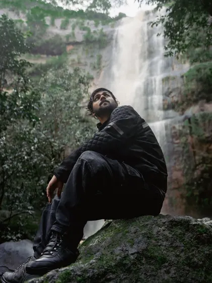 Photos of me embracing the monsoon, standing with arms outstretched in front of a waterfall and sitting contemplatively on a rock. These images convey a deep connection with nature.