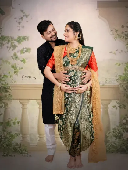 An intimate couple portrait in traditional attire. The husband gently holds his wife's baby bump, creating a moment of connection and love against a classic backdrop.