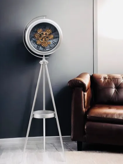 Here is the silver tripod clock shown in a room setting next to a leather sofa. Its clean lines and metallic finish provide a cool, contemporary contrast to the warm leather.