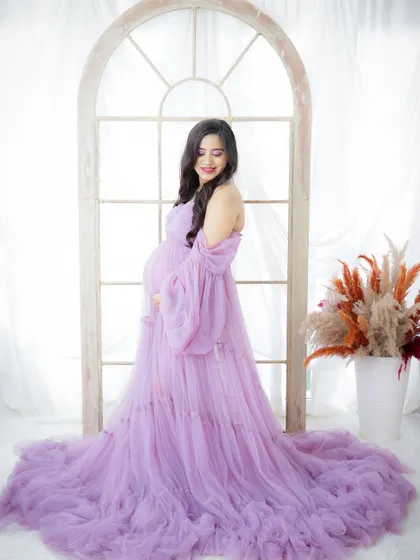 A dreamy and light-filled portrait. The mom-to-be stands by a window, her lavender tulle gown creating a soft and ethereal look.