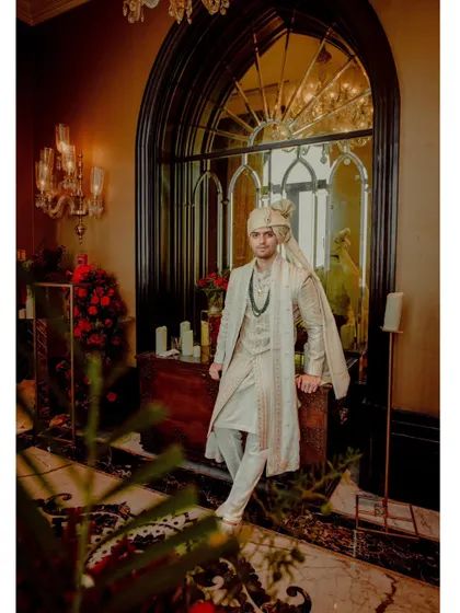 A full-length portrait of the groom in his elegant sherwani, posing in a grand, chandelier-lit hallway.