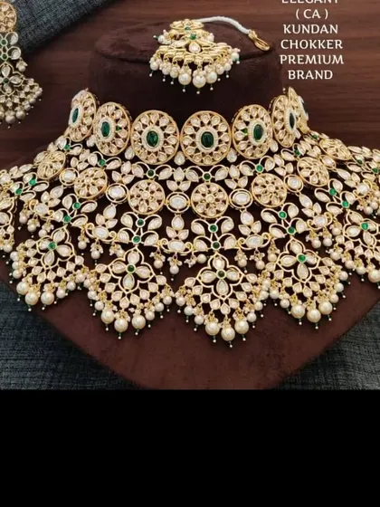 A premium bridal choker set available for rent. This piece features intricate floral motifs with green stones and pearl drops, and comes with matching earrings and maang tikka.
