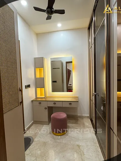A complete dressing area with a vanity table featuring a backlit mirror, a pink stool, and a large sliding wardrobe with striped glass panels.