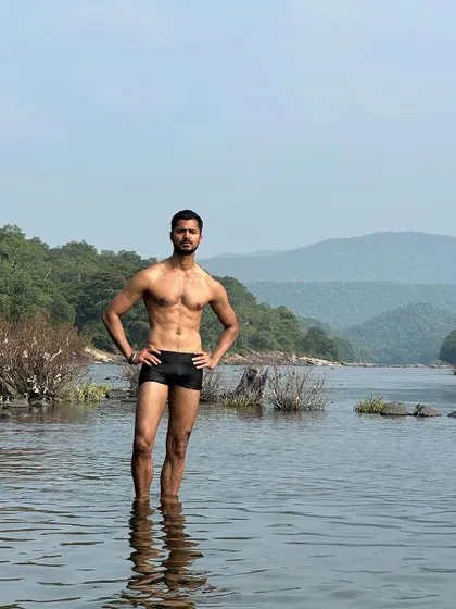 A confident, hands-on-hips pose in the water, showcasing a strong and balanced physique against a beautiful natural backdrop.
