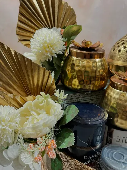 A close-up of our Glitterati gift hamper. This shot highlights the intricate brass burner and candle, paired with white floral accents and golden palm leaves for a touch of art deco glamour.