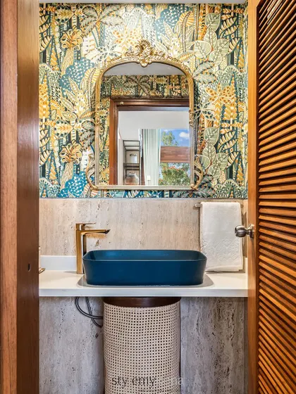 A front-on view of the powder room, highlighting the cane-detailed vanity basket and bold wallpaper.