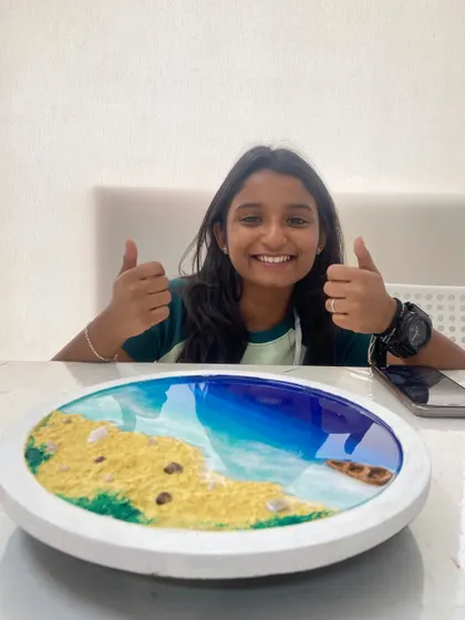 The finished product. A student gives a thumbs up, thrilled with the resin beach art she created. Our workshops are designed to ensure everyone leaves with a piece they are proud of.