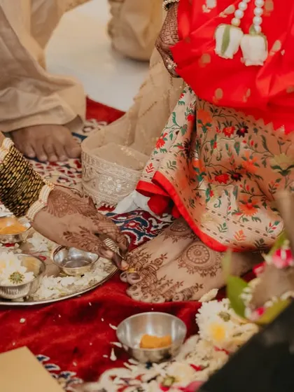 A close-up of a traditional foot-washing ritual, highlighting the cultural details and beautiful henna on the bride's feet.