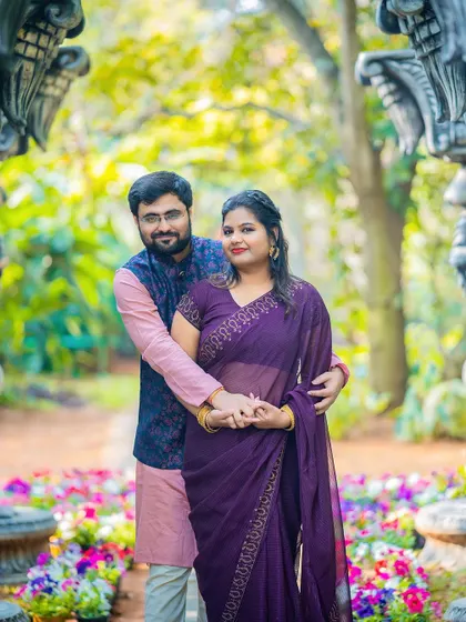 A sweet embrace between a couple, framed by ornate pillars and a garden path.