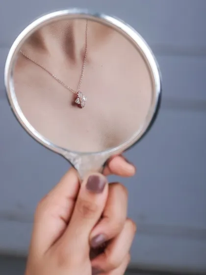 A creative and artistic shot showing a necklace's reflection in a hand mirror. This unique perspective is engaging and highlights the product in a memorable way for marketing campaigns.