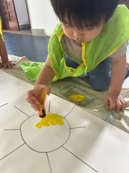 Using a paint dabber, this young artist carefully fills in the outline of a sun. This tool helps develop hand-eye coordination and control.