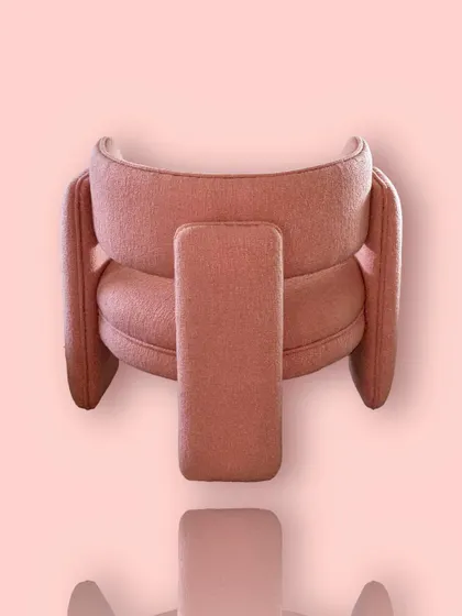 The back view of the coral bouclé "Pebble" chair, revealing its unique three-legged structure and compact, sculptural form.