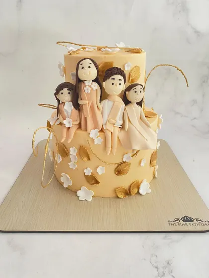 A truly personalized cake featuring custom fondant figurines of the entire family. This two-tiered cake is decorated with gold leaves and white flowers, making it a heartwarming centerpiece.