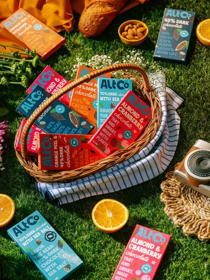 A vibrant picnic scene featuring Alt Co. chocolates in a basket surrounded by fresh oranges. The bright, sunny lighting and colorful setup create a feeling of joyful, outdoor indulgence.