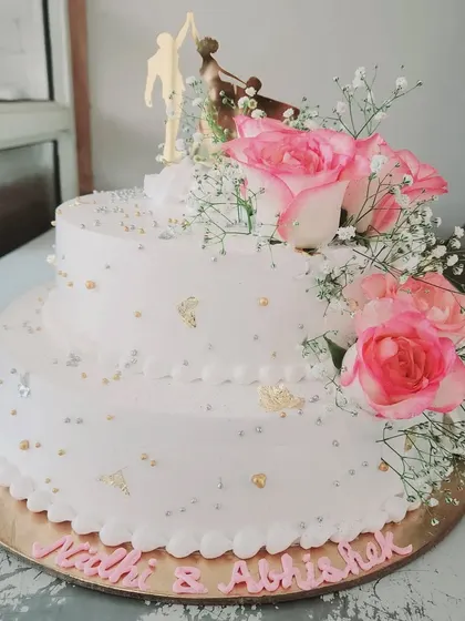We love the festive vibes of wedding season. This two-tier engagement cake is adorned with fresh pink roses and a romantic couple topper, creating a beautiful centerpiece for the happy couple.