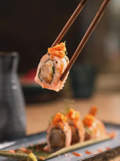 A beautifully lit shot of a sushi roll held by chopsticks. The focus on the glistening topping and ingredients inside makes it look incredibly appetizing, ideal for Japanese restaurant photography.