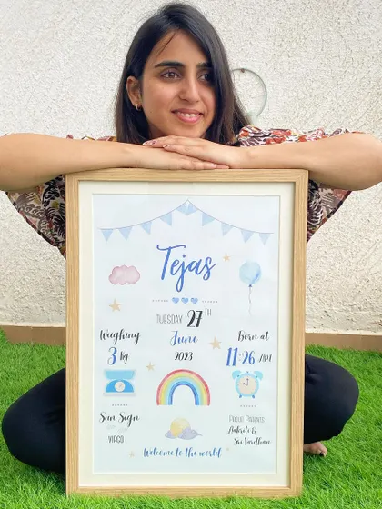 I love holding the finished product. Here I am with a framed baby biography for Tejas, featuring a blue color scheme with a balloon and rainbow. It’s so rewarding to create these special keepsakes for new parents.