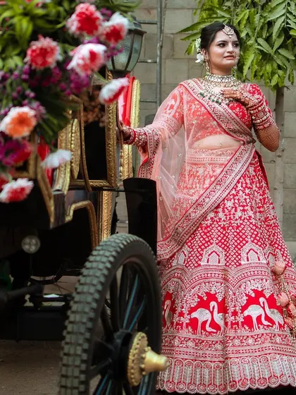 This bride looks like she stepped out of a fairytale, posing next to a floral carriage in her stunning red lehenga.