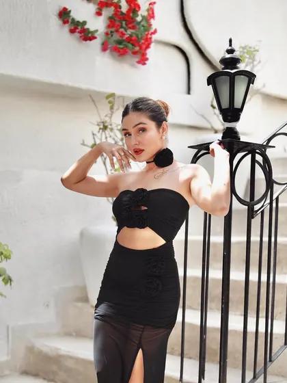 A softer portrait from the black dress shoot, with the model posing by a staircase, highlighting the floral details on the outfit.