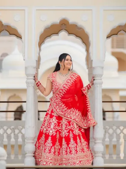 The bride poses on a palace balcony, her red lehenga spread out beautifully. She looks like royalty in this stunning portrait against the arched architecture.