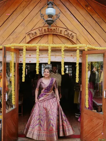 The bride's stunning entrance, framed by the rustic wooden doors of the venue and traditional marigold garlands.