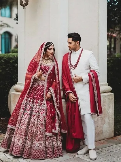 A classic red and white coordinated look for the bride and groom. The bride's intricate red lehenga perfectly complements the groom's elegant white sherwani and red stole.