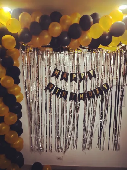 A black and yellow balloon arch against a silver tinsel curtain for a home birthday party.
