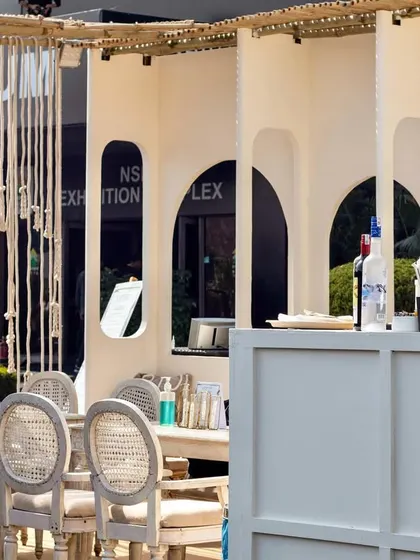 A wider view of the Cafe Tesu pop-up, showing the seating area with cane-back chairs and the service counter. The design combines white textured walls with natural wood and rope elements for a boho feel.