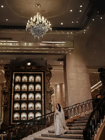 A wide shot that captures the scale and grandeur of the venue. The bride on the staircase is the focal point, but the towering, ornate interior adds a sense of fairy-tale luxury.
