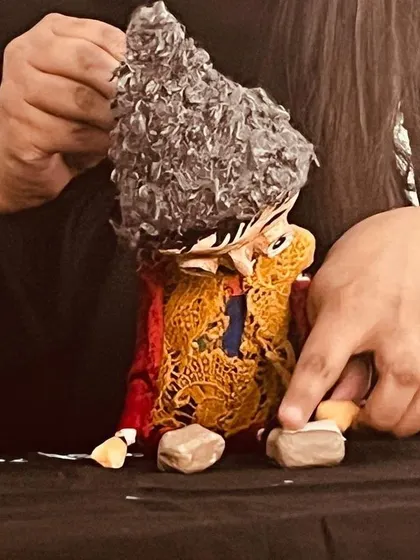 A close-up of a handmade puppet with detailed clothing and curly hair, being prepared for a show at the Snehadhara Foundation.