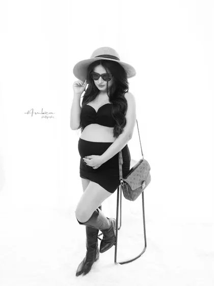 A fun and fashionable black and white portrait with a playful attitude. The styling with the hat, sunglasses, and boots shows that maternity photography can be trendy and full of personality.