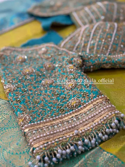 The sleeve of the teal blouse, with dense embroidery and bead tassels.