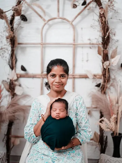 A mother proudly presents her newborn to the world. She holds her peacefully sleeping baby, both looking towards the camera, in a classic and heartfelt portrait.