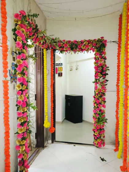 A simple yet festive entrance decoration for a home engagement or pooja. The door frame is decorated with garlands of bright pink and yellow artificial flowers.