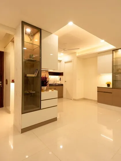 This foyer design uses glass and light to create a sense of openness. The strategically placed display cabinets act as subtle partitions, defining the space without closing it off from the adjoining kitchen and living areas.