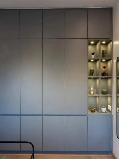 A full-height grey wardrobe with an integrated open display niche. The warm backlighting in the niche creates a beautiful focal point for displaying treasured items.