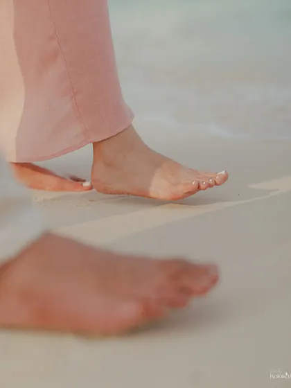A detail shot focusing on the couple's feet on the wet sand, telling a story of a romantic walk along the beach.