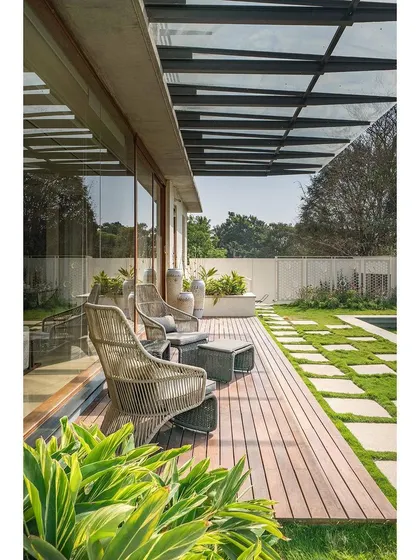 A wooden deck extends the living space into the garden, creating a perfect spot for relaxation. The glass roof provides shelter without obstructing the view, framing the outdoors as a key part of the home's design.