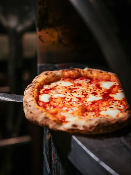 A perfect Margherita pizza on a peel, fresh out of the oven. The cheese is melted, the crust is golden and charred, and it's ready to be devoured.