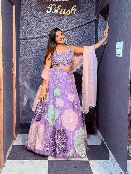 A full-length shot of a model in a unique lavender lehenga with large, colorful floral appliqué work.
