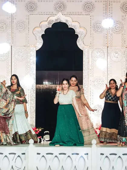 A vibrant group dance performance at the Sangeet. The intricately carved white stage backdrop adds a touch of traditional elegance to the festivities.