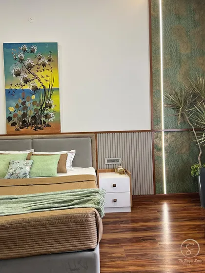 A master bedroom with an earthy color palette. The design features a grey upholstered bed, green and brown bedding, and a textured green accent wall with a vertical light strip, creating a calm and natural ambiance.